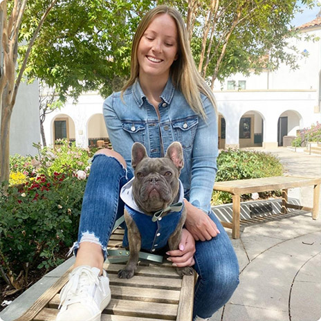 woman wearing denim jacket poses on a bench with french bulldog