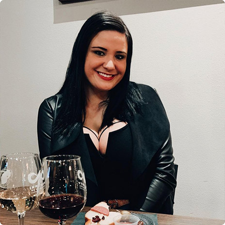 woman wearing black leather jacket poses at a table with wine glasses