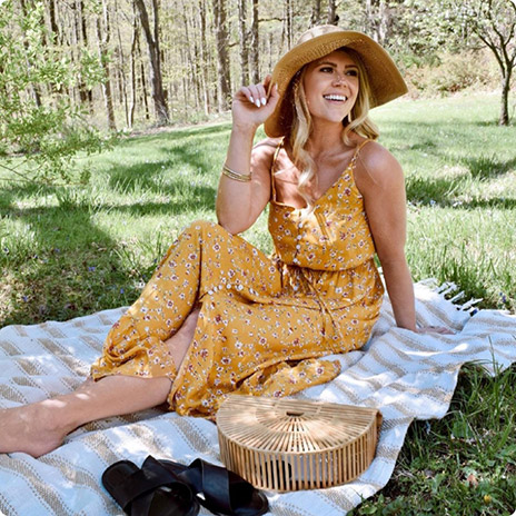 woman wearing yellow dress and straw hat sits on picnic blanket in grass